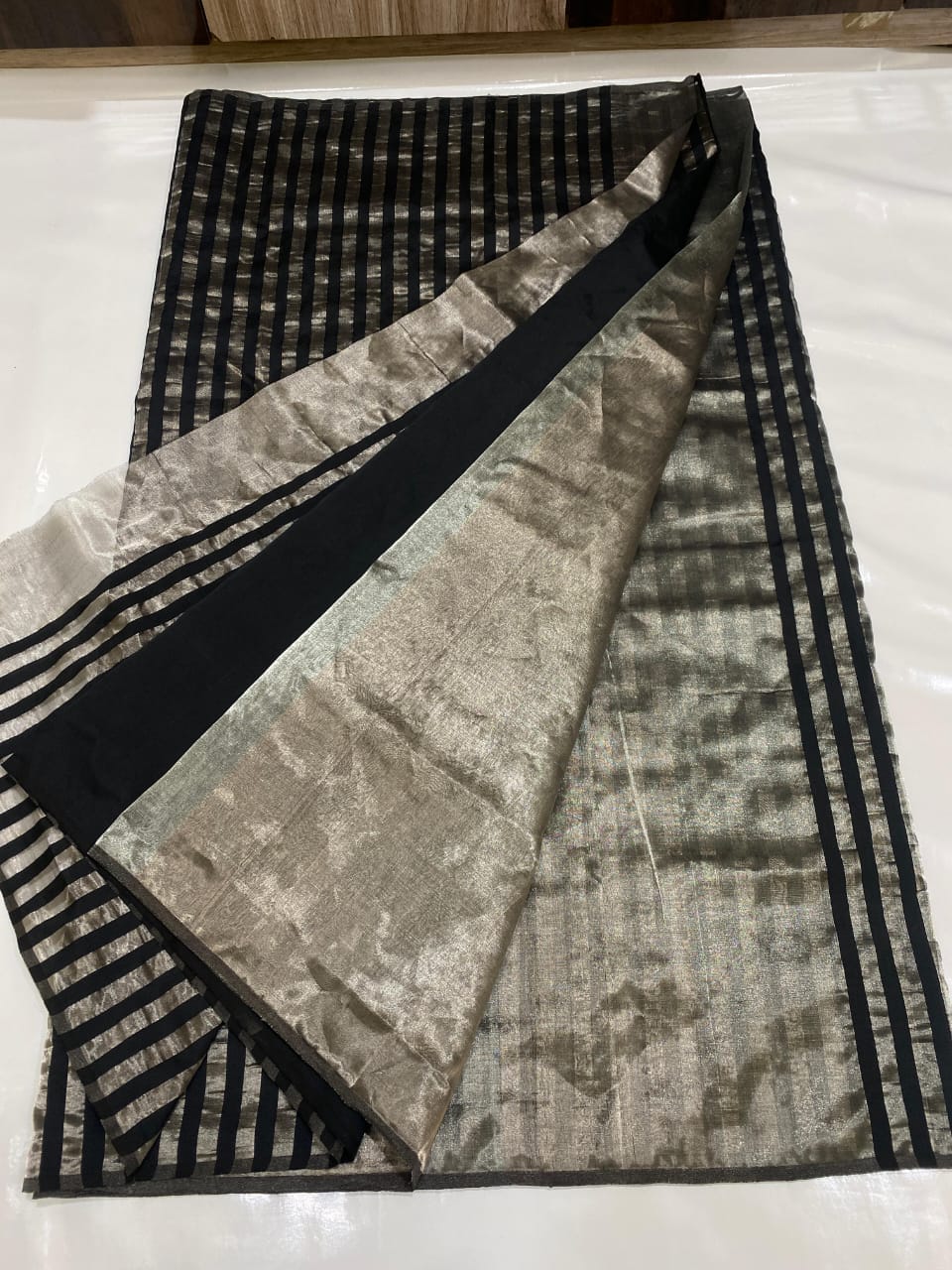 Silver Chanderi Handloom Pattu Tissue Silk Saree With Elegant Black Striped Weaving, Rich Tissue Finish, Stylish Woven Border And Matching Blouse Piece.